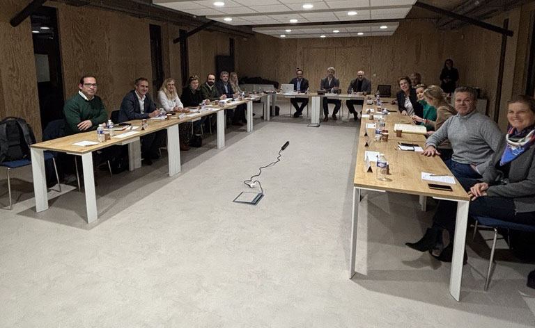 Photo d'une réunion du conseil avec des participants assis autour de deux longues tables en U dans une salle de conférence.